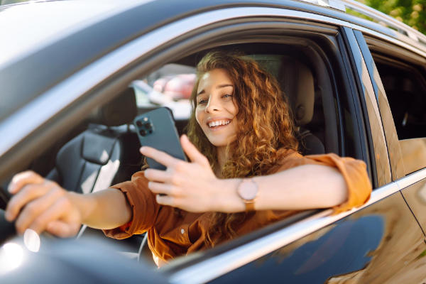 Young woman looking at her phone while driving, a common distraction for young drivers